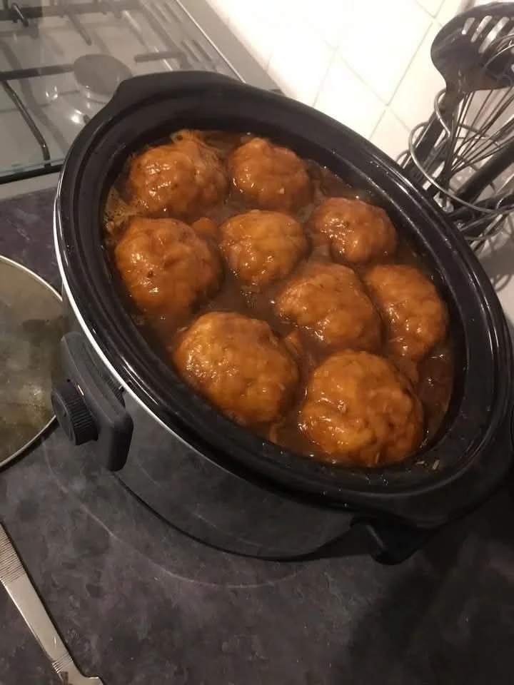 A bowl of savory beef stew with dumplings, garnished with herbs.