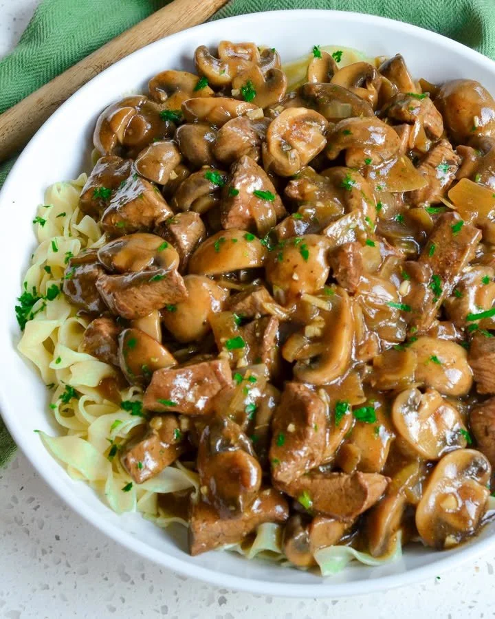 A bowl of beef noodles topped with fresh herbs and vegetables.