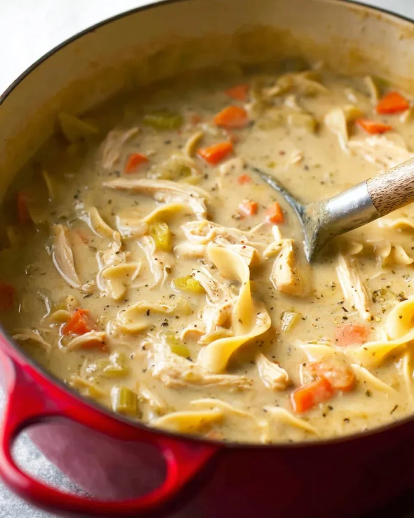 Creamy chicken noodle soup garnished with herbs in a white bowl