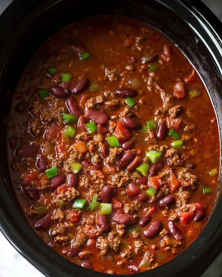 Delicious bowl of slow cooker chili topped with cheese and fresh herbs.