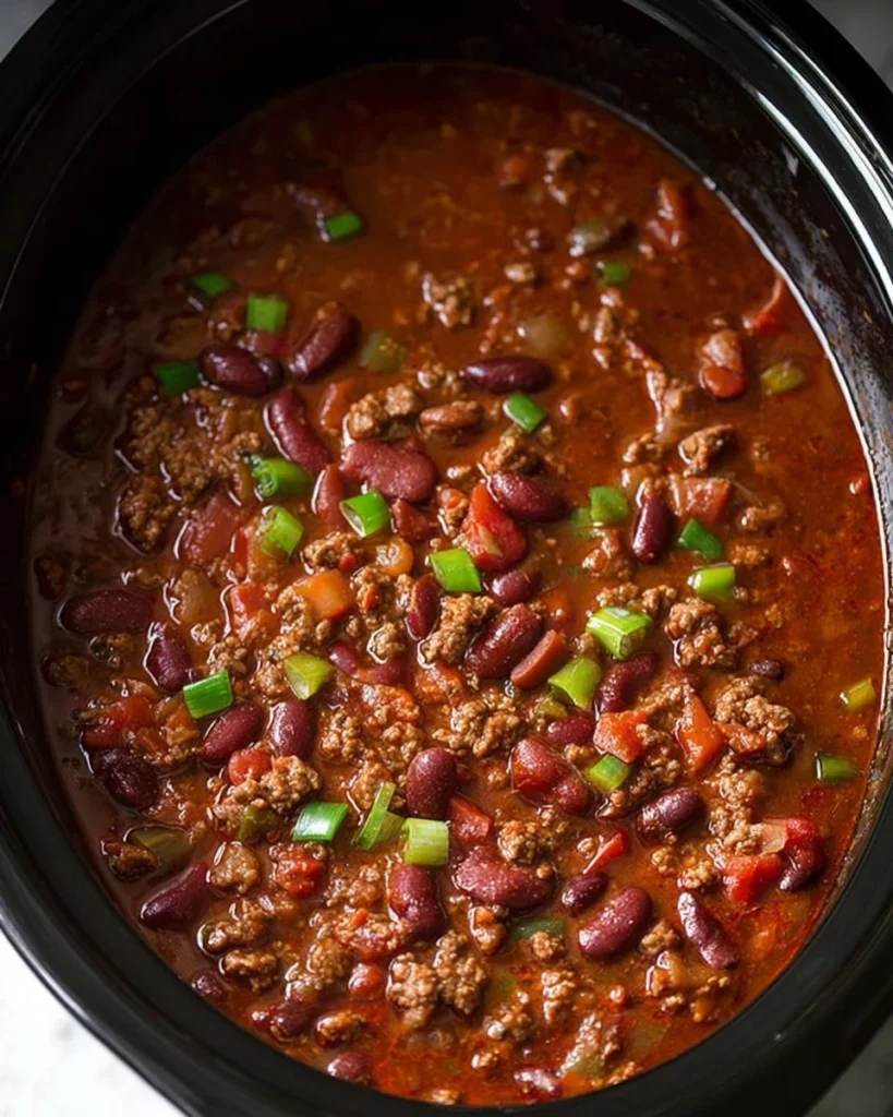 Delicious bowl of slow cooker chili topped with cheese and fresh herbs.