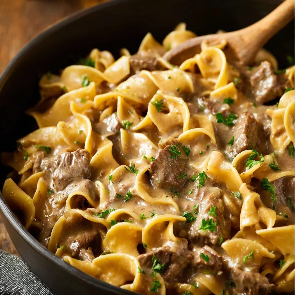 Bowl of creamy Beef Stroganoff garnished with parsley and served over egg noodles.