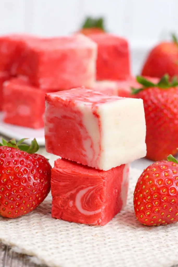 No bake strawberry swirl fudge topped with fresh strawberries on a white plate.