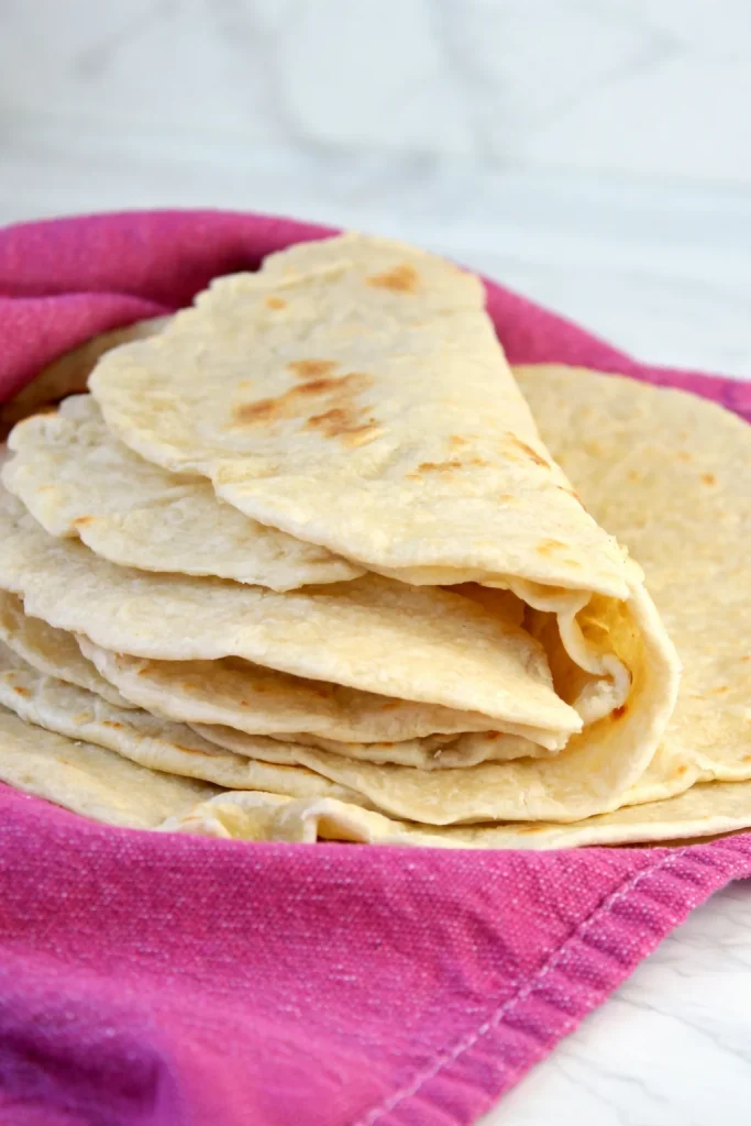 Homemade flour tortillas stacked on a rustic wooden table