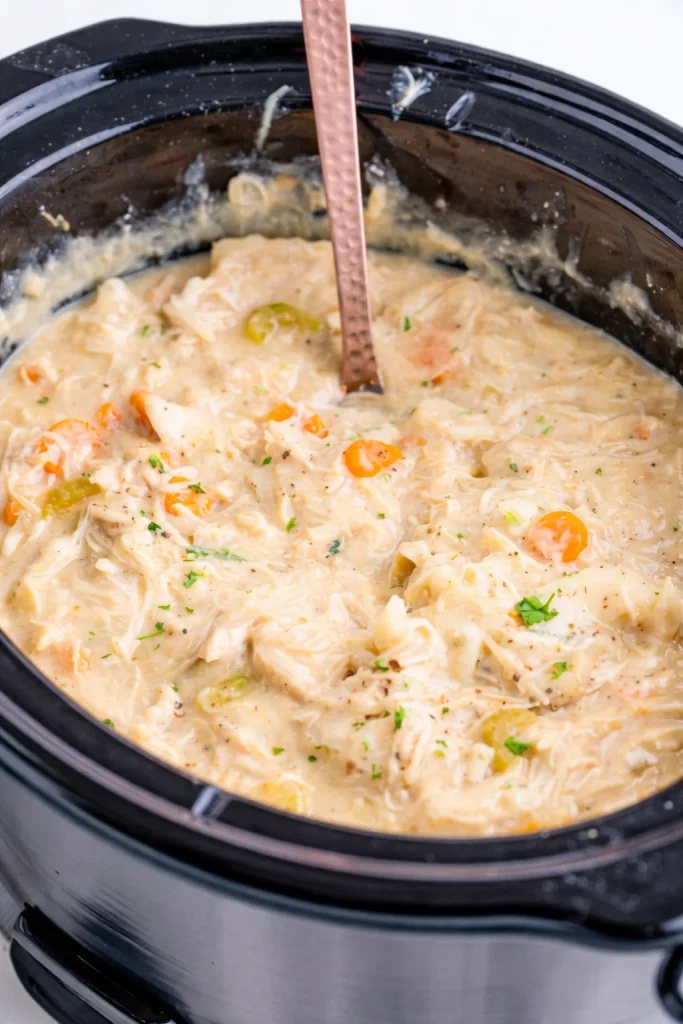 A bowl of slow cooker chicken and dumplings with vegetables and herbs.