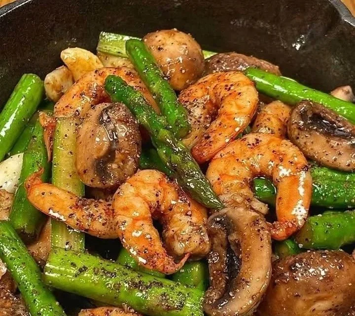 Stir-fried shrimp with asparagus and mushrooms served in a vibrant dish.