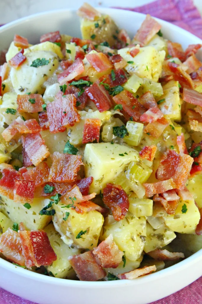 Bowl of zesty German potato salad garnished with herbs.